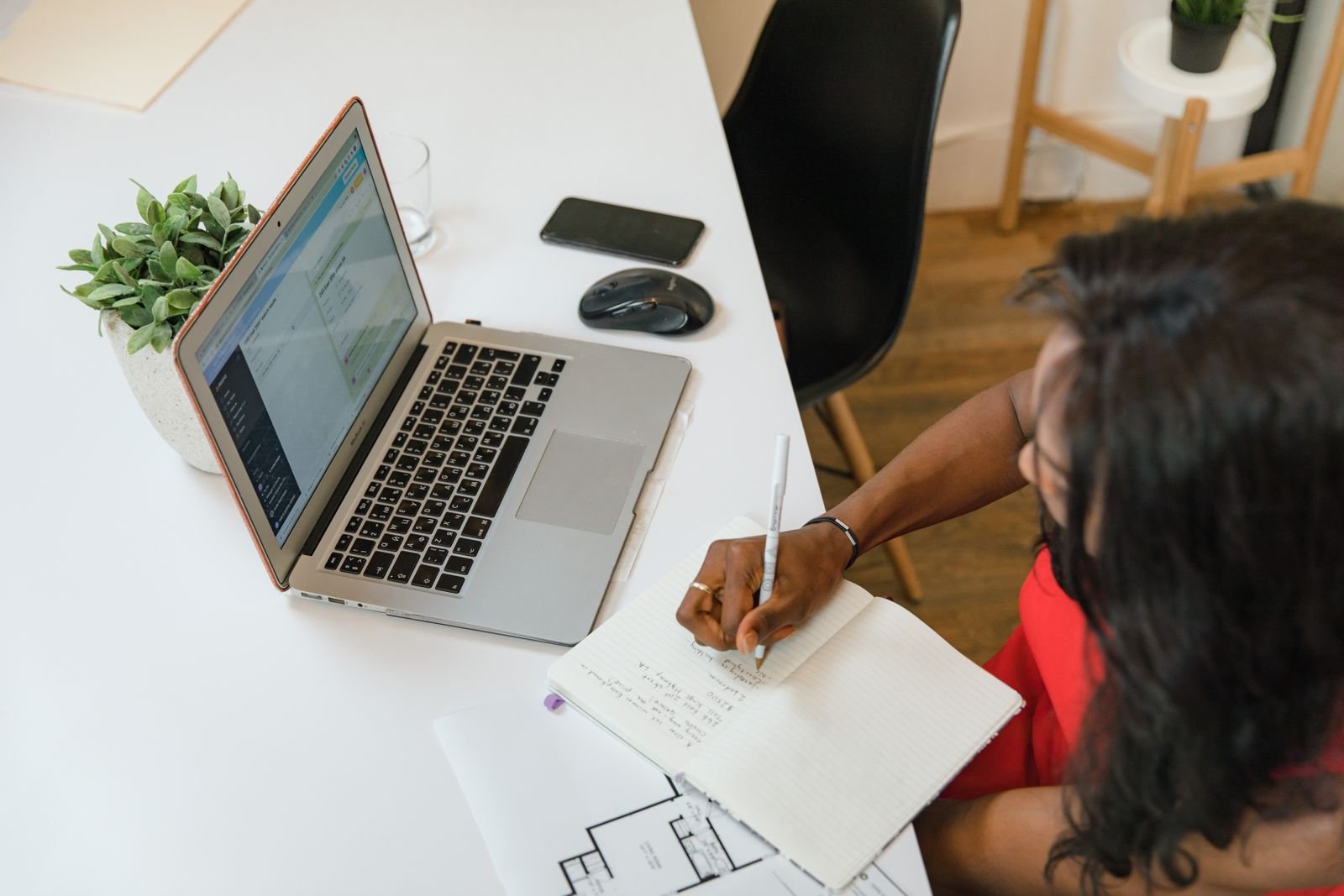 Businesswoman writing in a notebook at an office desk next to a laptop